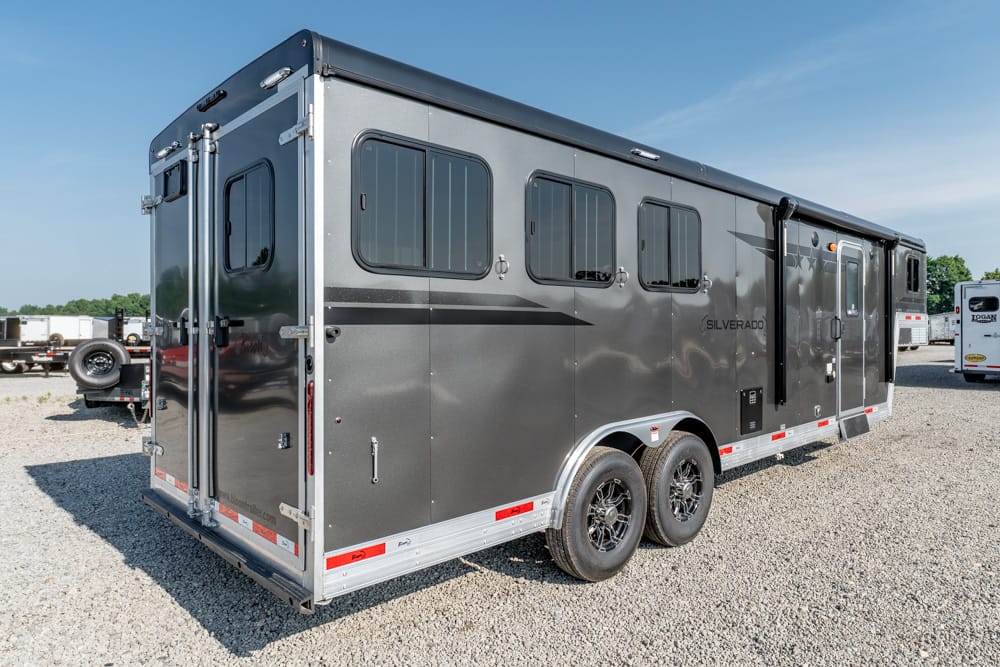 Long dark gray Silverado horse trailer with three side windows, a side door, and dual axles on a gravel lot