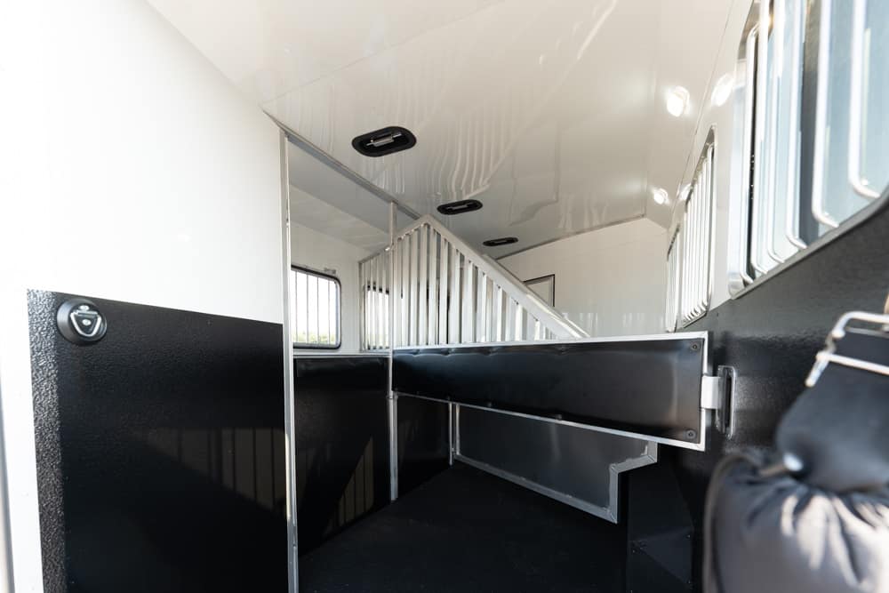 Interior of a horse trailer showing a metal divider, black lower walls, and small windows with bars along the side