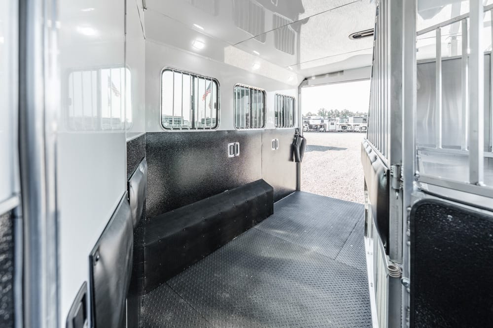 Interior of a white horse trailer with side windows, black rubber floor, and metal walls.