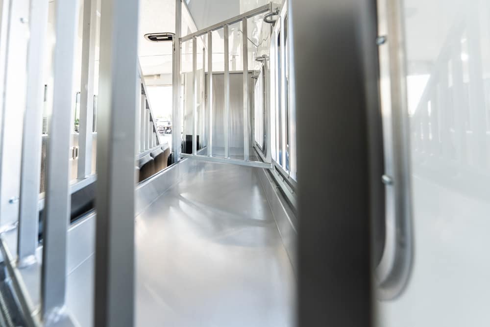 Empty stainless-steel bus interior with metal railings along the aisle and windows on the side, viewed from near the back toward the front.