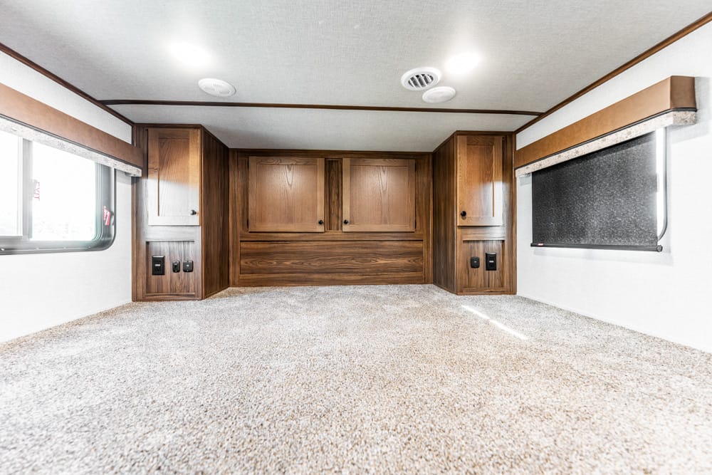Wooden cabinets and storage compartments inside an RV bedroom with carpeted floor.