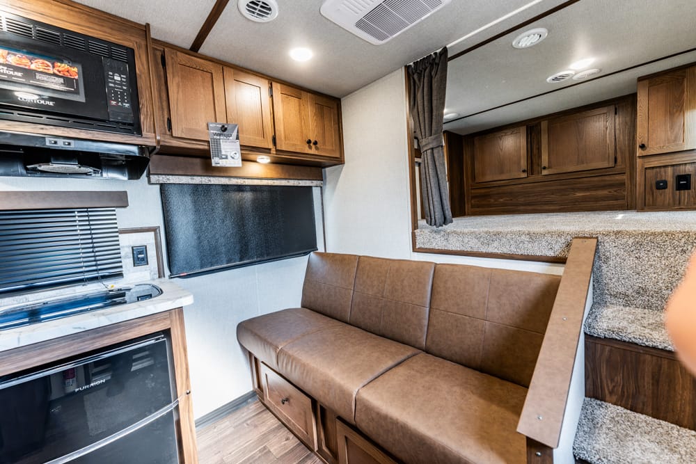 Interior of a compact RV living space with a brown leather sofa, wood cabinets, microwave, and small fridge.