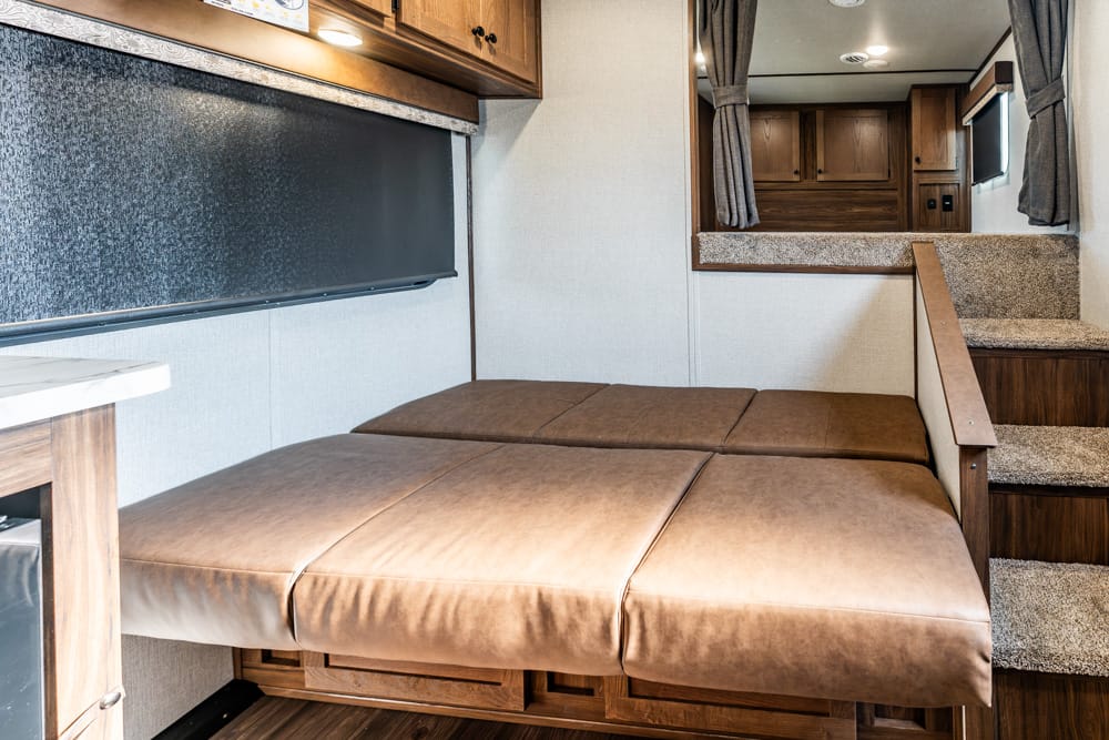 Interior of a recreational vehicle: a brown leather sofa bed with storage underneath, wood cabinets, and a countertop.