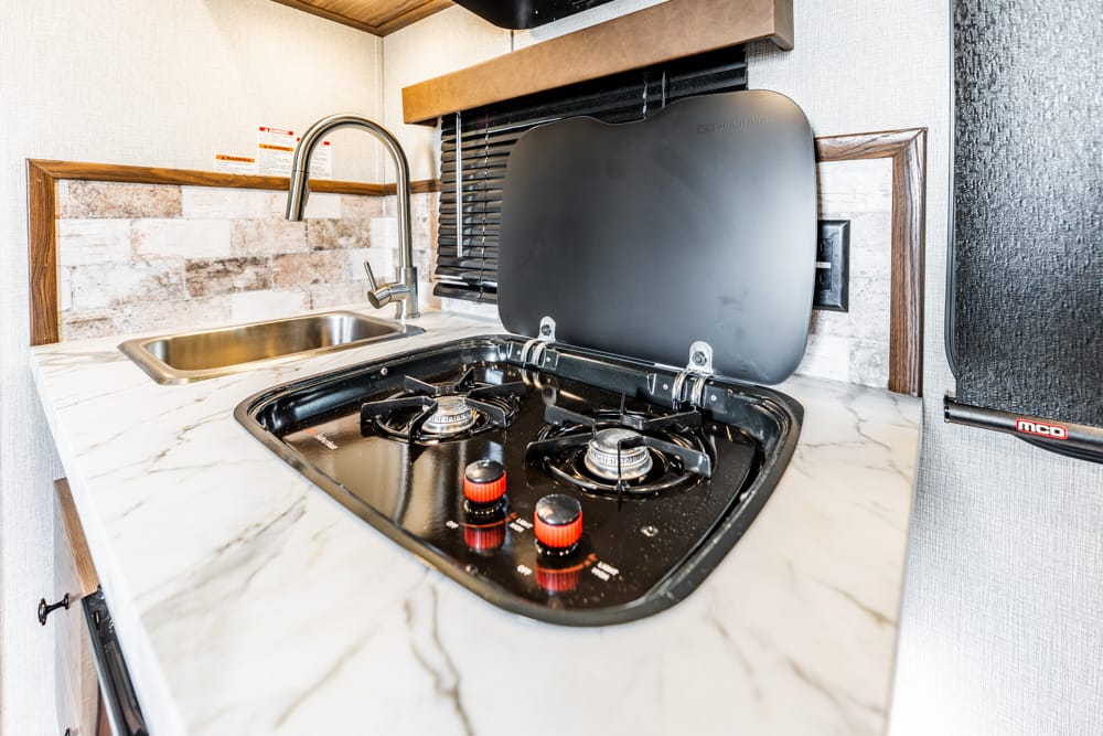 RV kitchenette with a two-burner gas stove and a compact sink on a marble countertop in a small galley set-up
