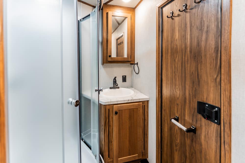Small bathroom with a wooden vanity cabinet, sink, and mirror, next to a glass shower enclosure on the left.