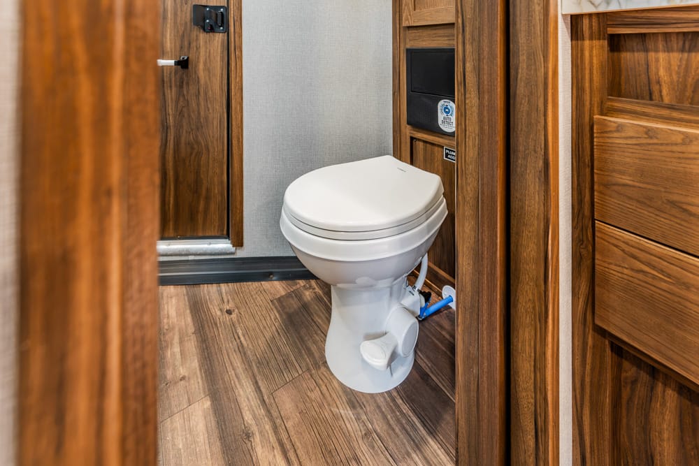 White toilet in a small wood-paneled bathroom with brown cabinetry and wood-look flooring.