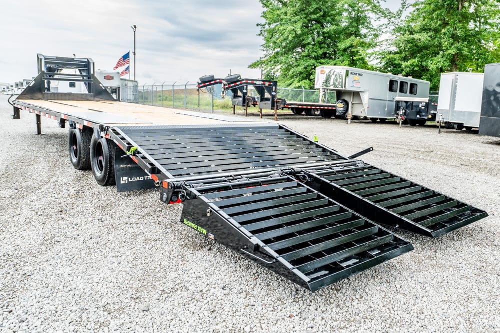 Long black car hauler trailer with fold-down ramps on a gravel lot