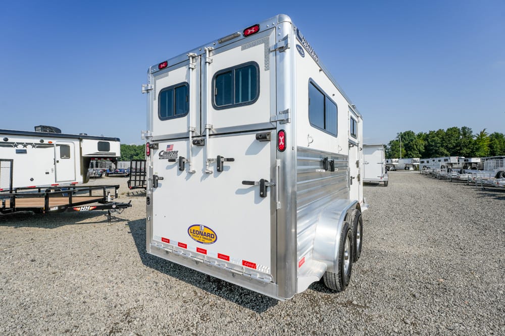 White two-axle horse trailer with rear double doors, side window, and aluminum trim in a gravel lot.