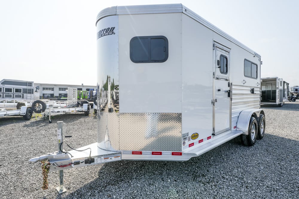 White tandem-axle enclosed trailer with diamond-plate front parked on a gravel lot among other trailers at a yard.