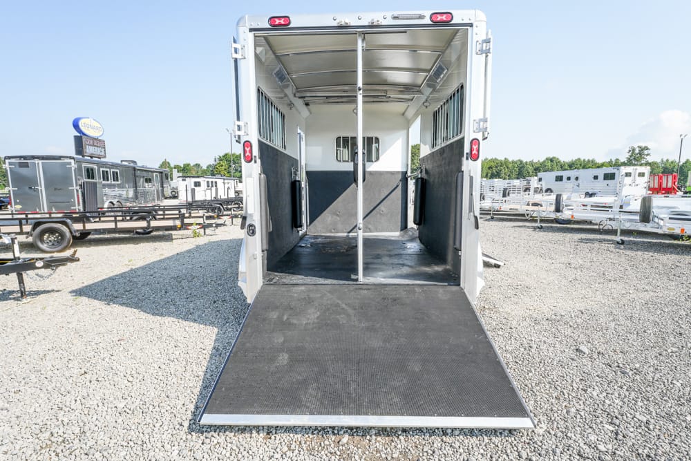White horse trailer with a lowered ramp, showing interior stalls and center divider on a gravel lot