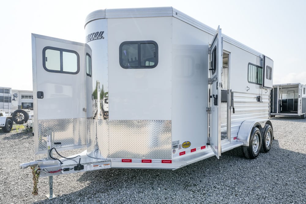 White tandem-axle horse trailer on gravel with rear and side doors open, diamond-plate front protection and hitch at the front.