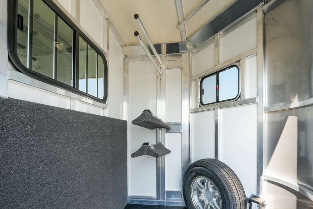 Interior of a metal trailer showing a mounted spare tire, two gray shelves, and a window on the side wall.