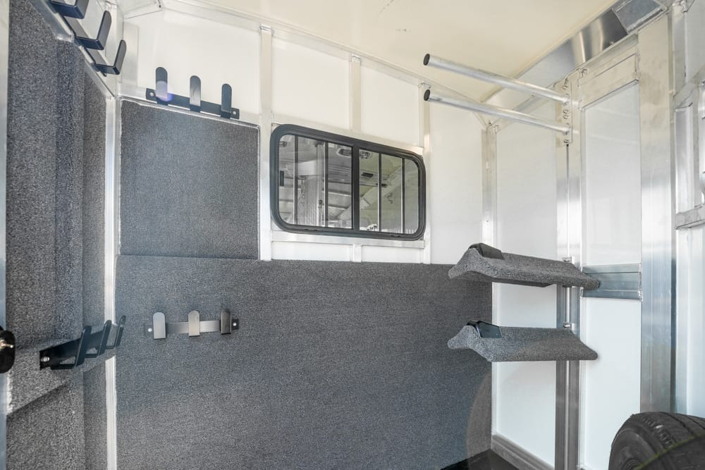 Interior of a metallic trailer with gray padded walls, a small window, and mounted hooks for gear storage.