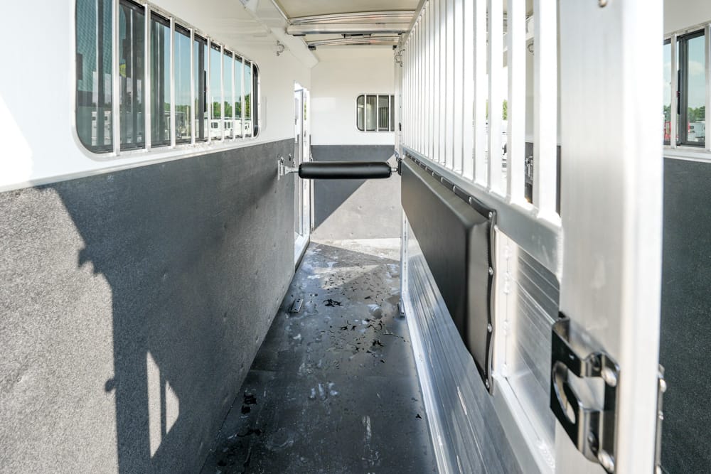 Interior of a horse trailer: narrow aisle with multiple windows along the left wall and a padded divider on the right side.