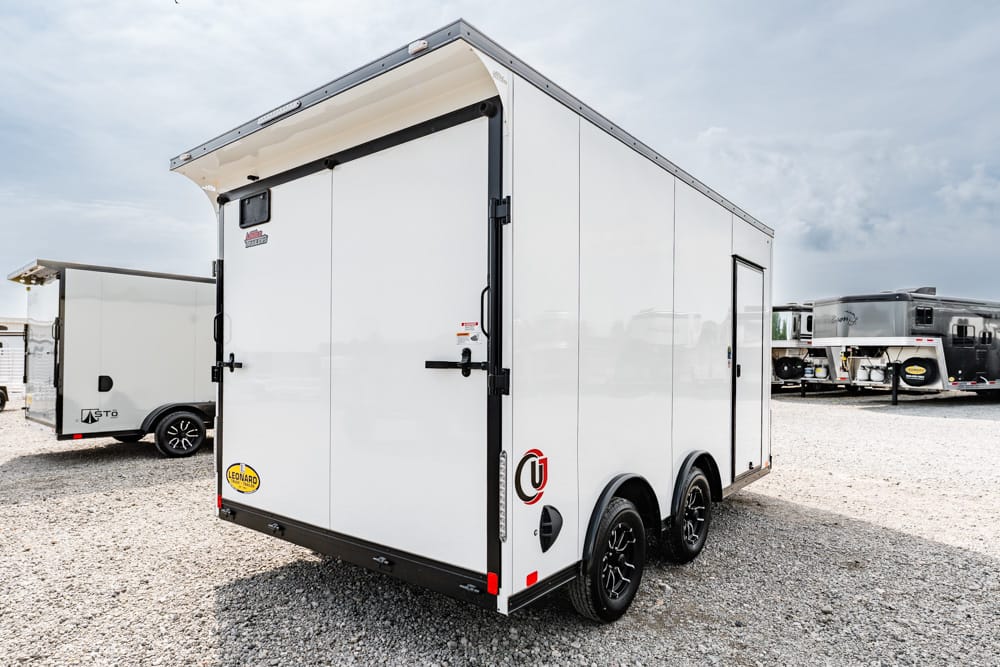 White enclosed dual-axle cargo trailer parked on a gravel lot with other trailers in the background.