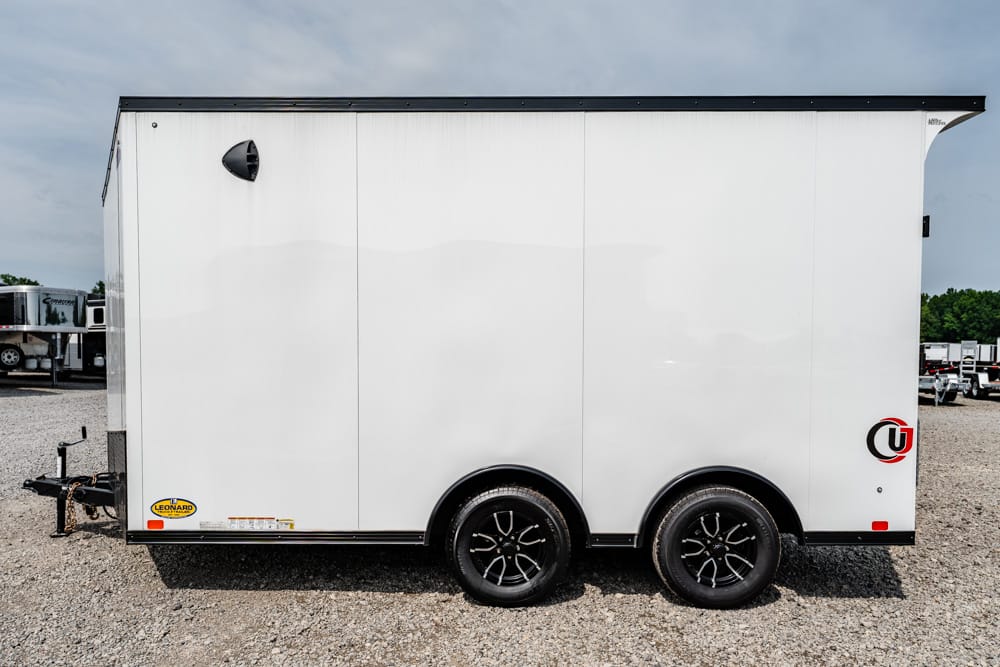 White enclosed dual-axle cargo trailer on a gravel lot, with black rims and a small front hitch, side view.