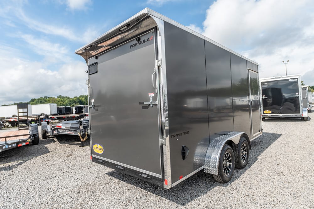 Gray enclosed cargo trailer with dual axles and aluminum fenders on a gravel lot