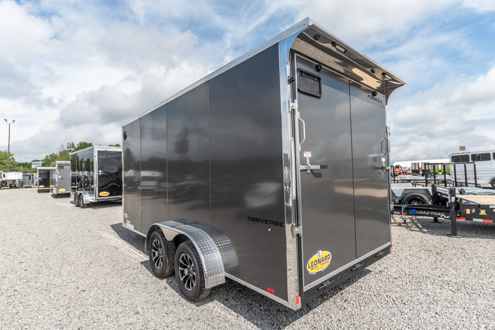 Dark gray, double-axle enclosed cargo trailer with diamond-plate fenders in a gravel lot.
