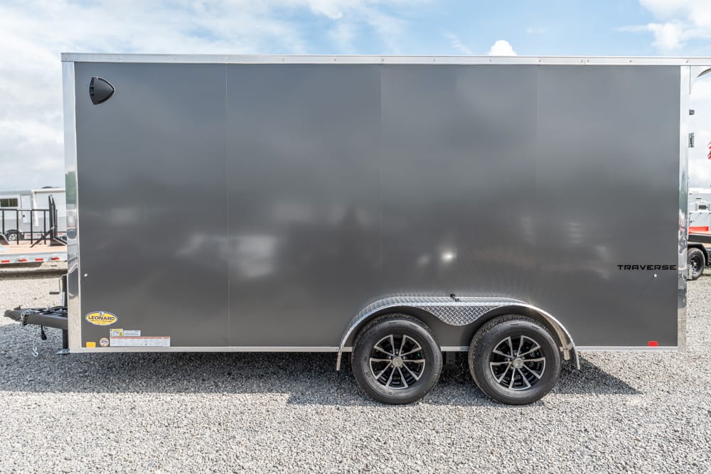 Grey tandem-axle enclosed cargo trailer on a gravel lot, with diamond-plate wheel wells and 'Traverse' branding on the side.