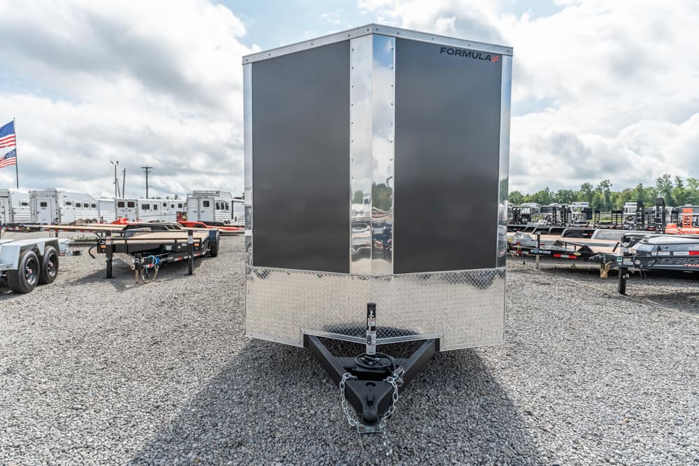Front view of a large enclosed cargo trailer with a diamond-plate lower front, parked on a gravel lot among other trailers.