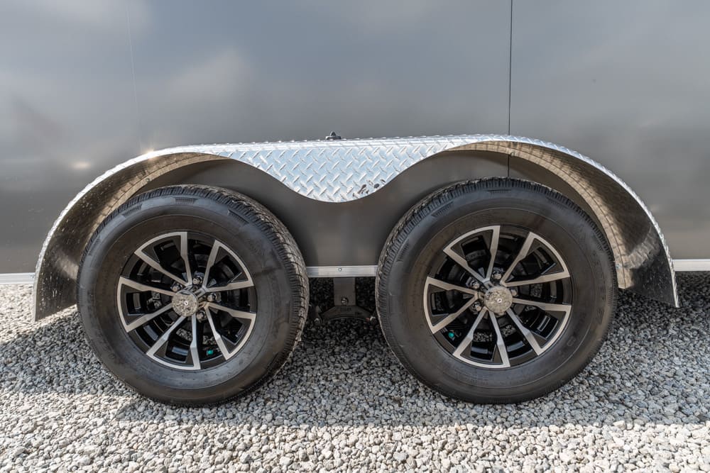 Dual-axle trailer with black alloy wheels and diamond-plate fenders on a gravel surface.