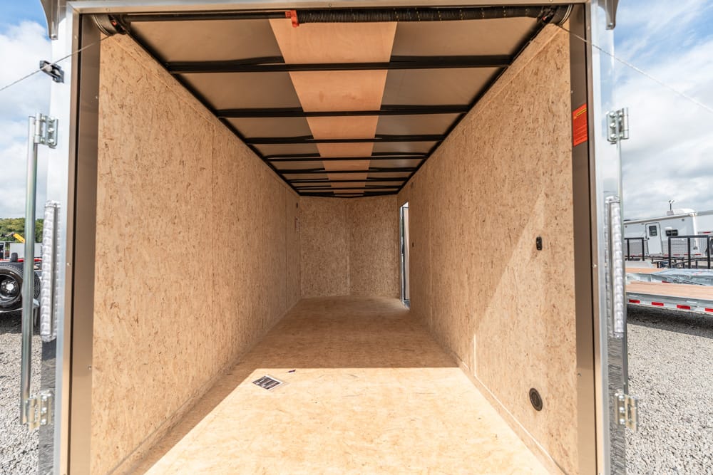 Empty plywood-walled cargo trailer interior, viewed from the open back doors toward the far end. (informative)