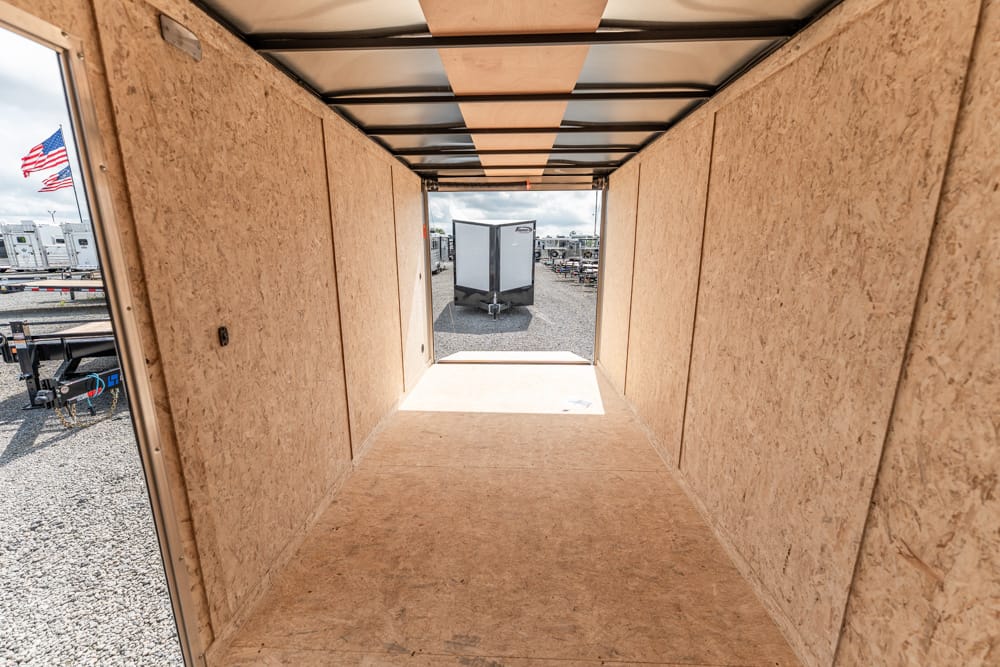 Wood-paneled trailer interior looking toward the open rear exit to a gravel lot with another trailer outside, and a flag visible outside left.