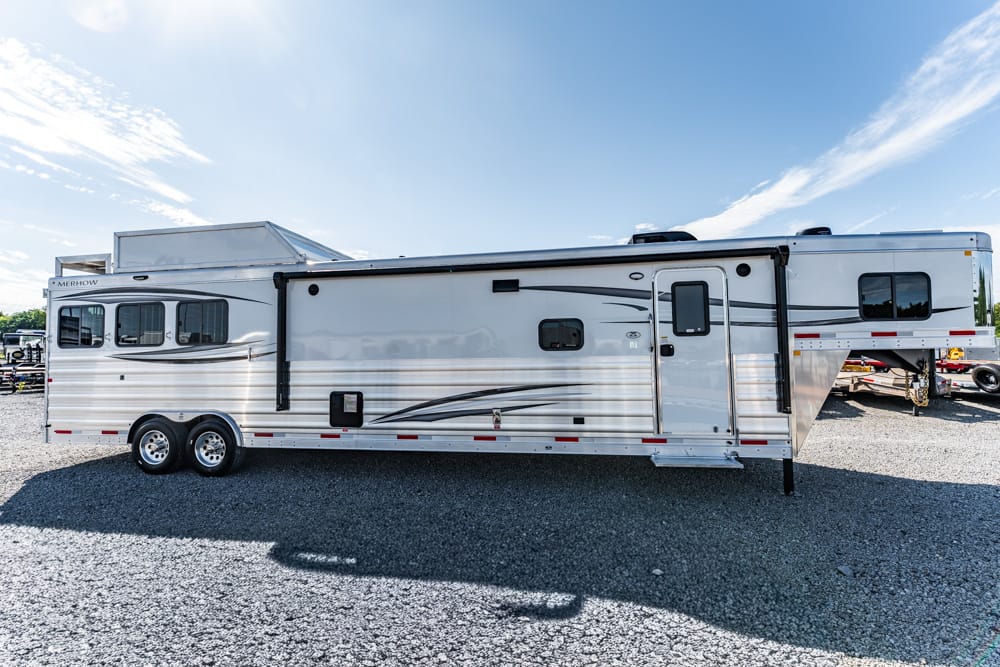 Large white fifth-wheel trailer with a side slide-out, parked on a gravel lot under a blue sky.