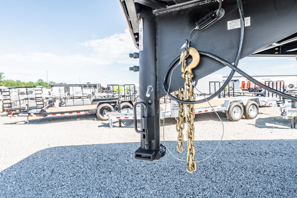 Gooseneck trailer hitch with safety chains and padlock on a gravel lot.
