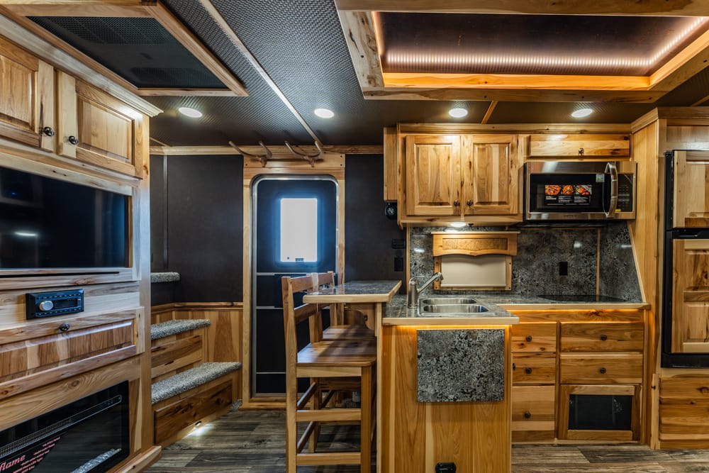 Wood-paneled RV kitchen with granite countertops, microwave, sink, and a small dining table with two chairs by the windowed door.