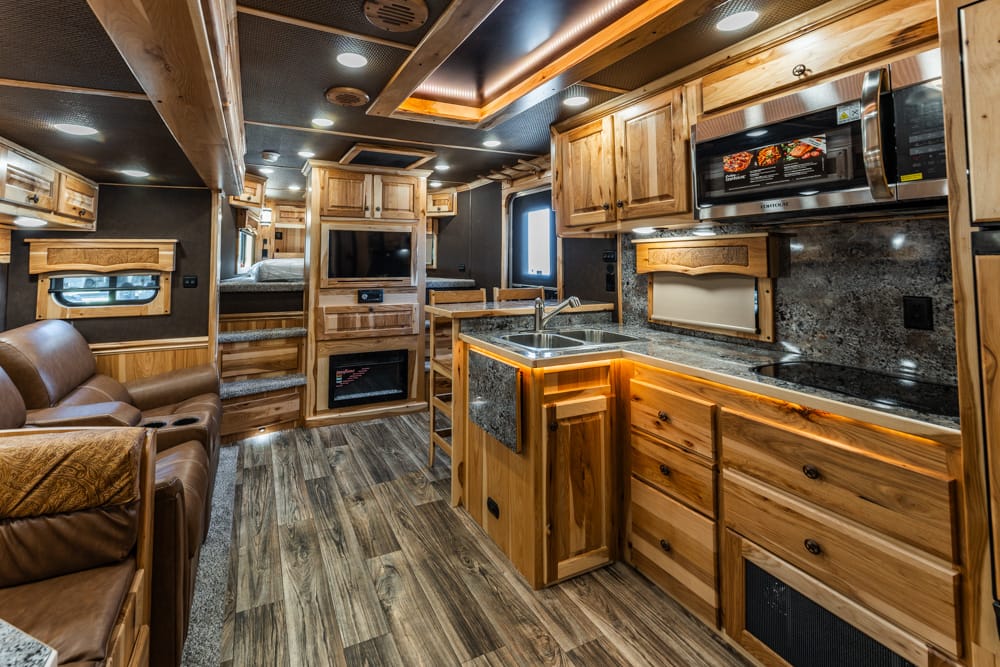 Wood-paneled RV interior with kitchen island, granite counters, microwave, and leather seating area.
