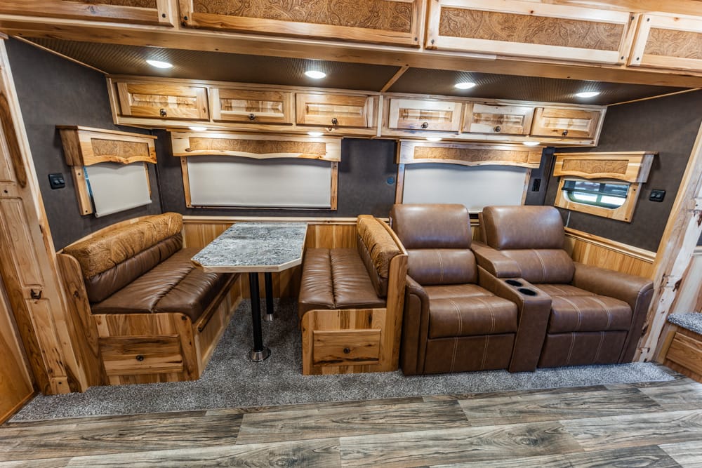 Wood-paneled RV living area with an L-shaped bench, marble-pattern table, and brown leather recliners on carpeted floor