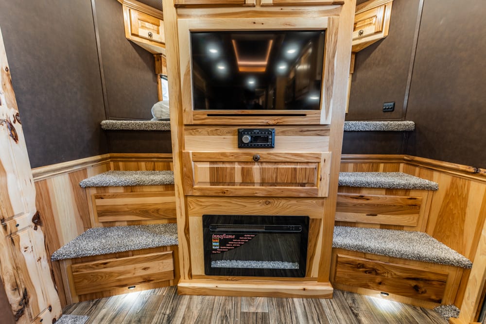 Wooden entertainment cabinet with a TV, central fireplace, and carpeted steps on both sides in a rustic interior.