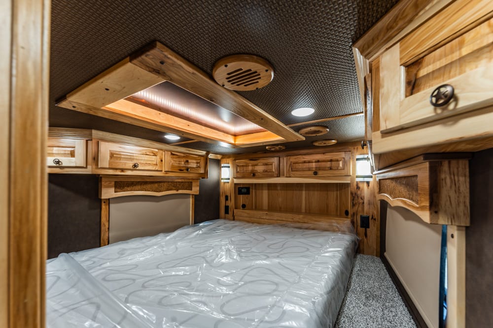 Wood-paneled bedroom in a cozy RV with a full bed, overhead cabinets, and warm built-in lighting for storage and comfort.
