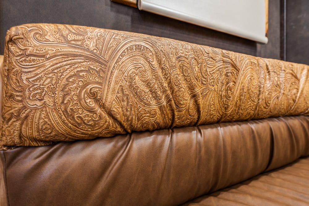 Close-up of a brown patterned cushion on a dark brown leather sofa, showing paisley-style fabric and soft folds.