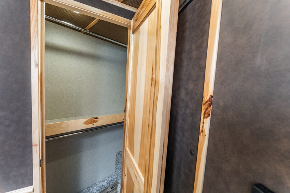 Open wooden closet frame with two metal clothing rods inside and beige-green walls.