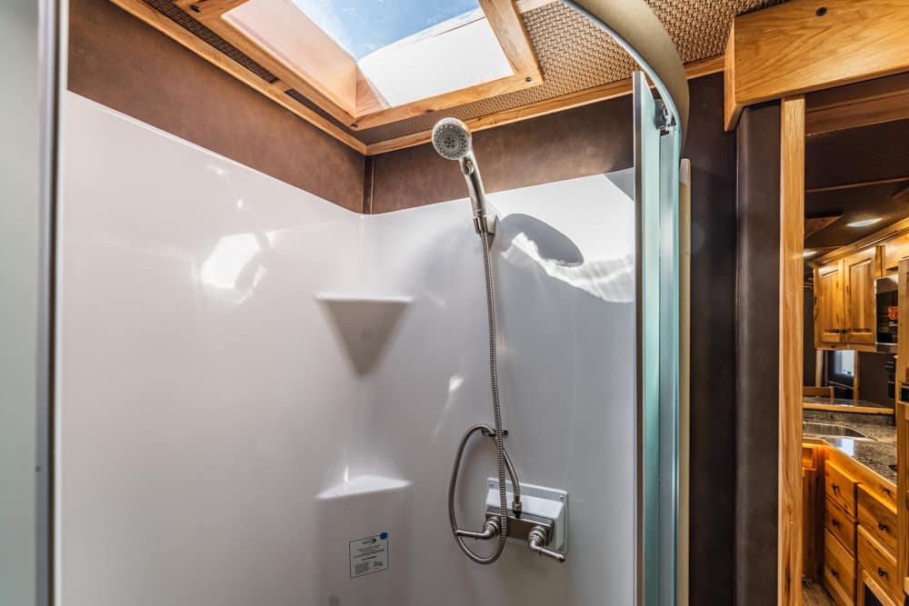 Shower stall with a handheld spray head and chrome faucet in a white surround, wood cabin accents visible nearby.