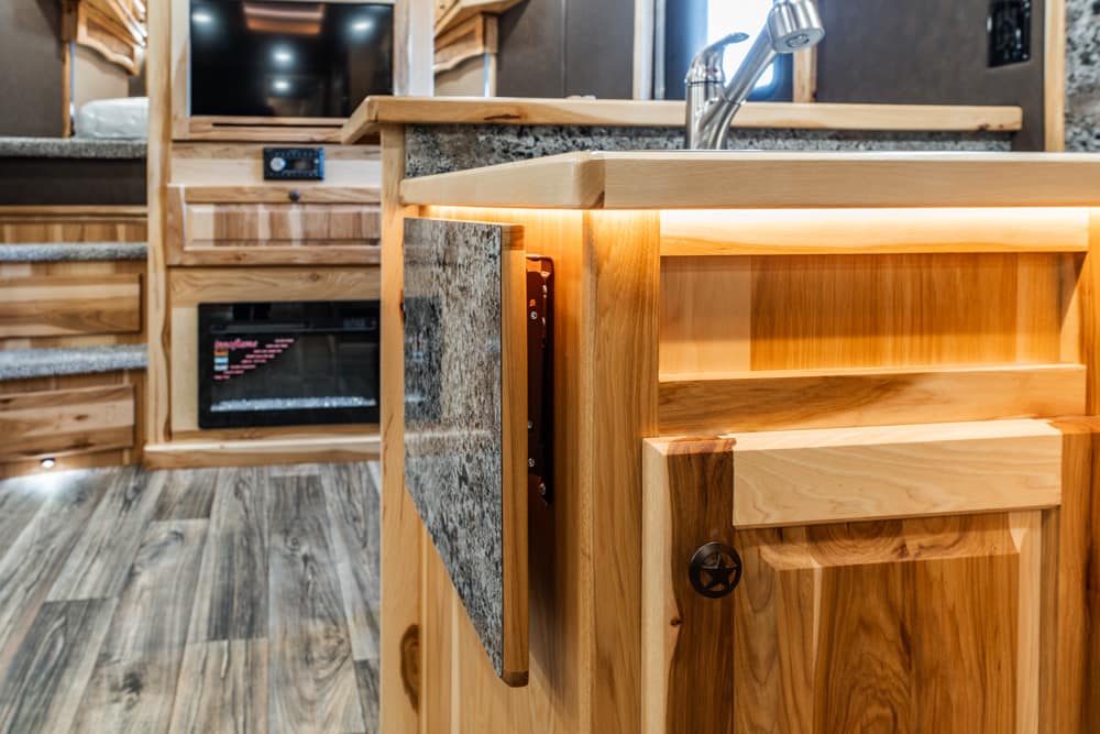 Wooden kitchen island with warm under-counter lighting and a stainless steel sink; granite countertop and cabinetry visible in the background.