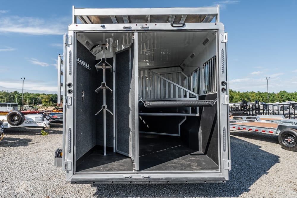 Interior of a horse trailer with divided stalls, saddle racks, and a rear storage area for gear.