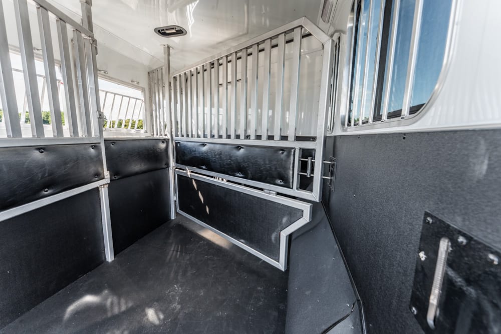 Interior of a horse trailer with metal dividing bars, black padded walls, and a rubber floor for stalls