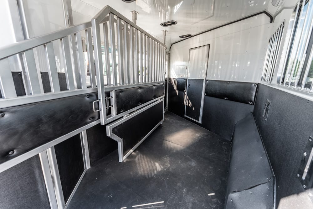 Interior of a horse trailer showing metal stalls, padded walls, and a center divider for horses.