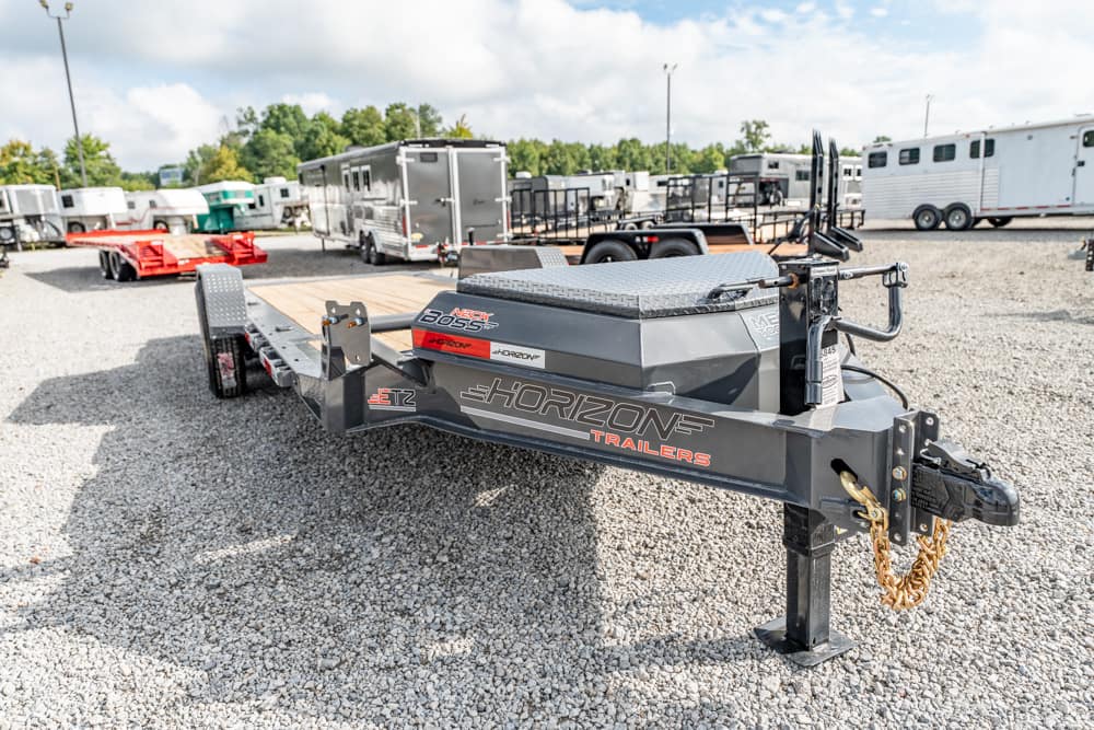 Gooseneck utility trailer by Horizon Trailers with a diamond-plate toolbox, parked on a gravel lot among other trailers and equipment.
