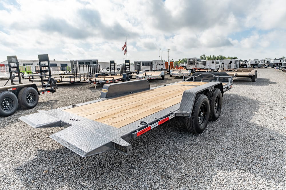 Flatbed trailer with a wood deck and dual axles in a gravel lot among other trailers.