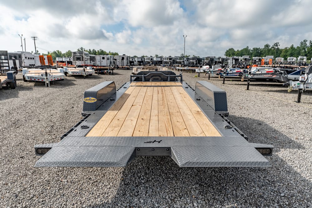 Flatbed trailer with wooden deck parked in a gravel lot among many other trailers on a sunny day