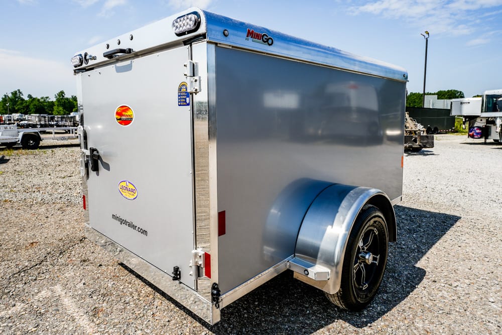 Enclosed silver cargo trailer on a gravel lot, featuring a black alloy wheel and curved fender in the foreground