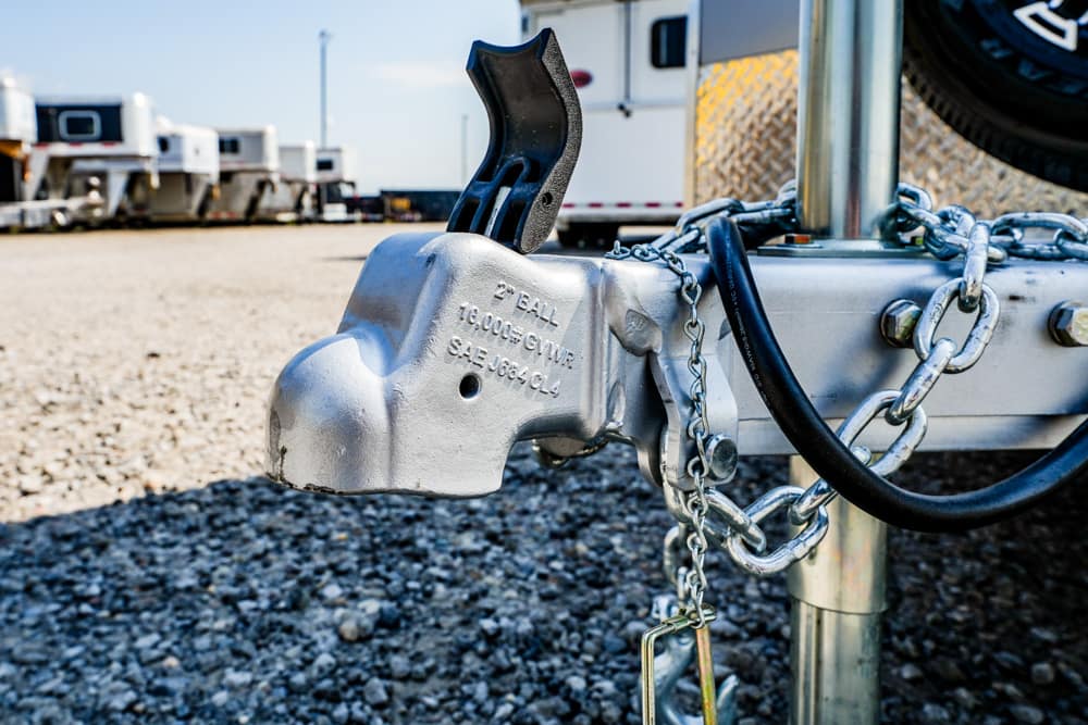 Close-up of a metal trailer hitch with safety chains and a black coupler at a campground trailer setup.