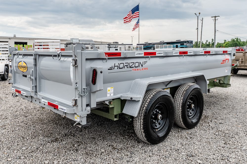 Gray Horizon dump trailer with tandem wheels on gravel, brand name visible and American flags in background