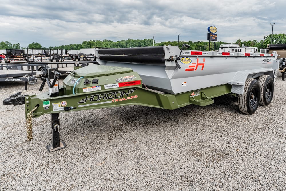 Side view of a green Horizon hitch and a large gray dump trailer with red Horizon logos, parked on a gravel lot with other trailers in the background.