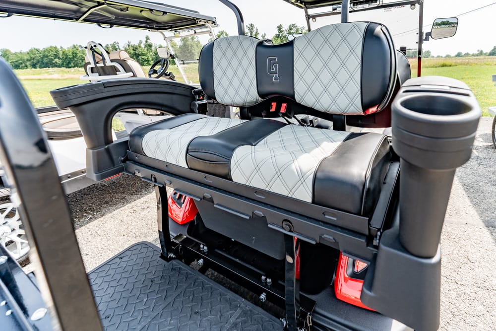 Rear-facing, cushioned seats with gray diamond stitching inside a golf cart, outdoors on a sunny course distance view behind.
