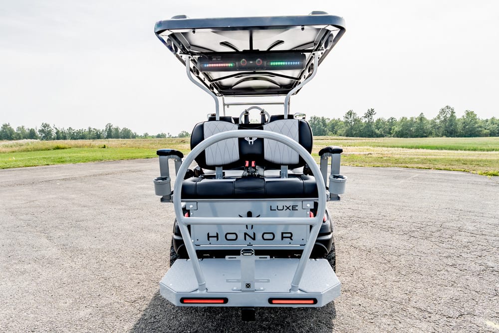 Rear view of a modern electric golf cart with two gray cushioned seats, roll bar, and LED lights, branded 'HONOR LUXE' on the back panel.